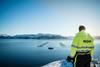 A worker dressed in a yellow high vis jacket is pictured overlooking a Mowi offshore fish farm