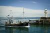Small fishing vessel next to a harbour wall with tiny lighthouse