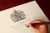 A hand holding a pen and writing on a royal warrant. Text says 'This is to certify that by command we have'