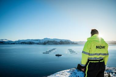 A worker dressed in a yellow high vis jacket is pictured overlooking a Mowi offshore fish farm