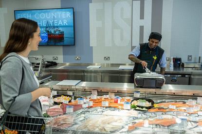 A shopper at a Waitrose fish counter with an employee weighing a seabass