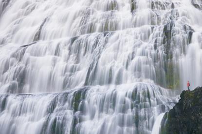 Very small person in red looking at a large waterfall