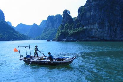 Vietnamese fishing boat with two fishers and cliffs in the background