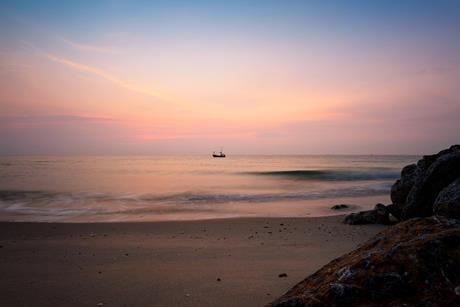 The picture shows a traditional fishing boat on water at sunrise
