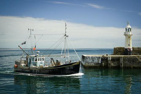 Small fishing vessel next to a harbour wall with tiny lighthouse