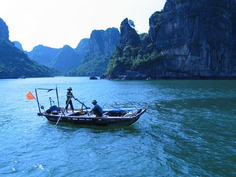 Vietnamese fishing boat with two fishers and cliffs in the background