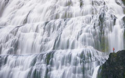 Very small person in red looking at a large waterfall