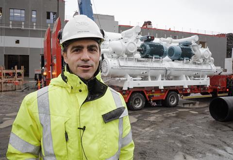 Arild Vikan, project manager at Salmon Evolution, in hi viz and hard hat standing in front of a heat pump being transported on a lorry