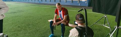 Erling Haaland sitting on a bench at a football stadium being filmed for an ad campaign by the Norwegian Seafood Council